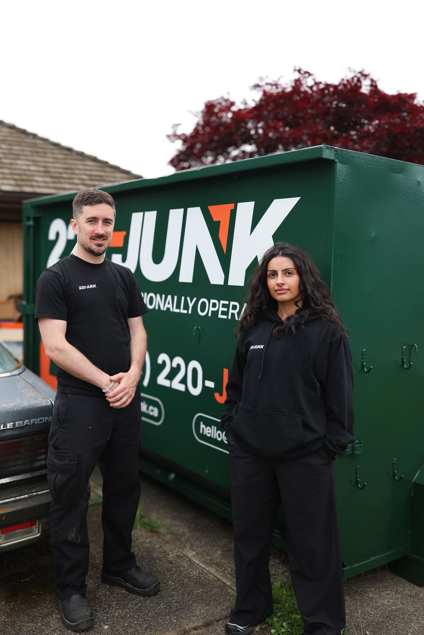 Two 220-JUNK team members standing in front of a green dumpster bin